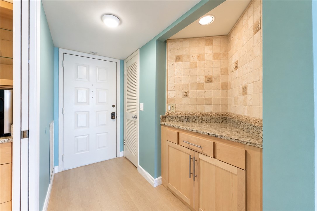 Light wood-finish flooring with a built-in cabinet featuring a light stone countertop and a tiled backsplash