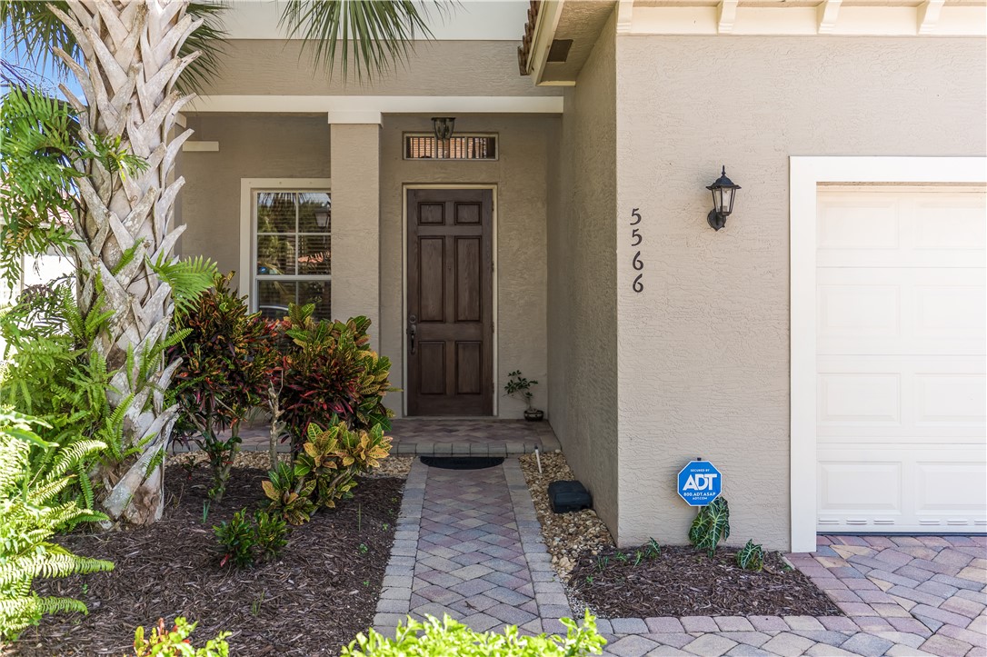 Stucco exterior with a paver walkway, mature landscaping, paneled front door, and an attached garage