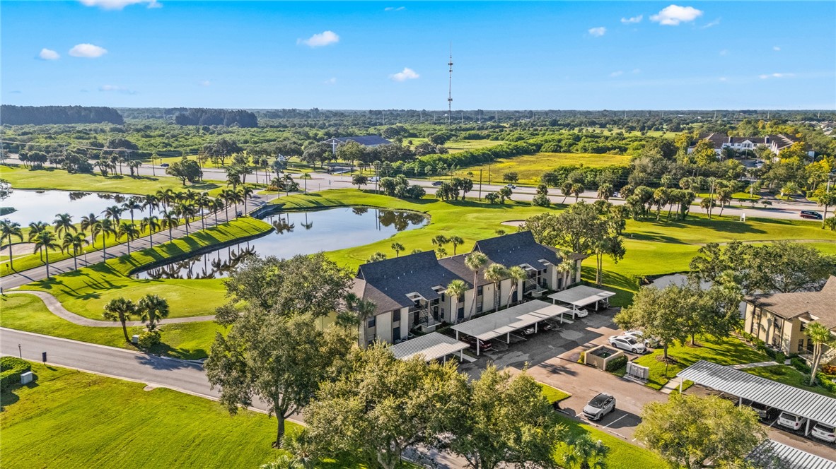 Manicured green spaces with mature trees, natural water features, a paved roadway, and covered parking structures