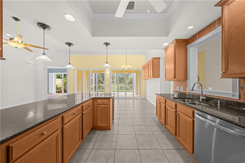 Spacious kitchen featuring wood cabinetry, dark countertops, a stainless steel dishwasher, tile flooring, and a tray ceiling with recessed lighting