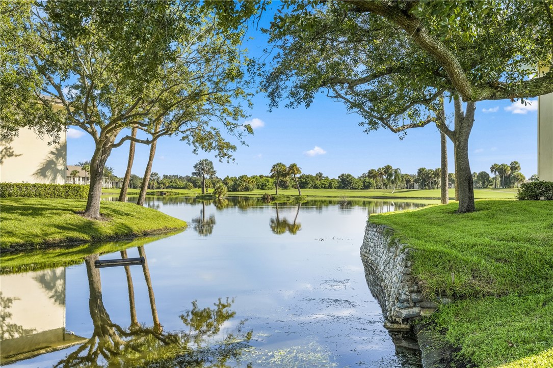 Expansive waterfront setting featuring mature trees, manicured grassy areas, and a stone retaining wall along the water's edge