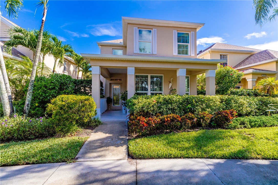 Two-story residence featuring a covered front entry with columns, mature landscaping, and a concrete walkway