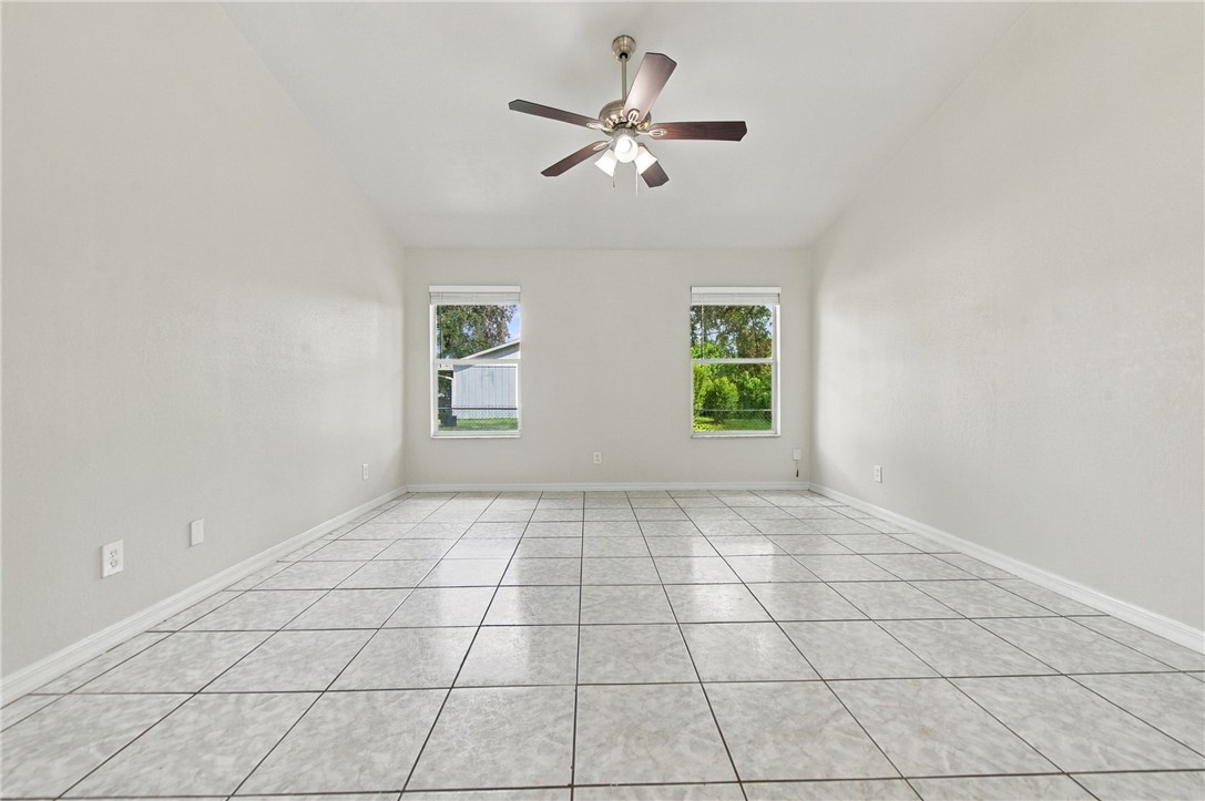 Spacious room featuring light-toned tile flooring, two windows, and a ceiling fan with integrated lighting