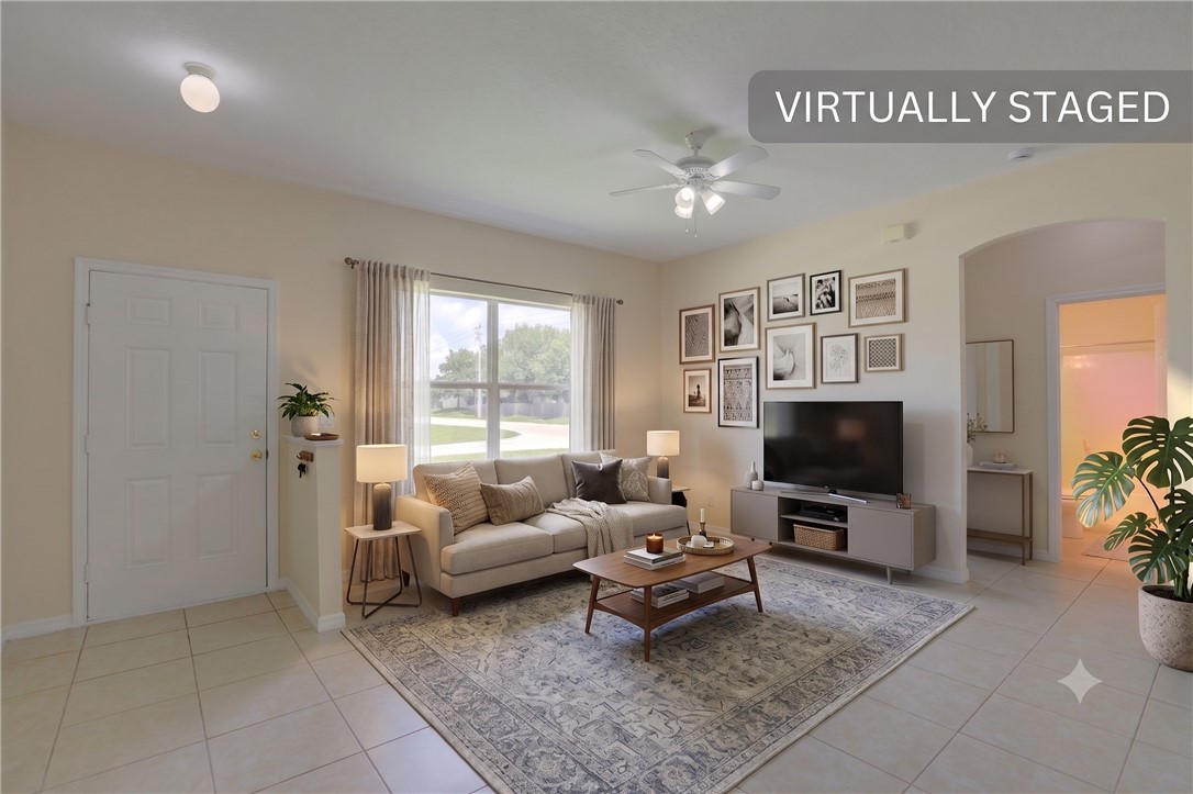 Living area featuring neutral wall paint, tile flooring, a window with exterior views, an arched doorway, and a ceiling fan