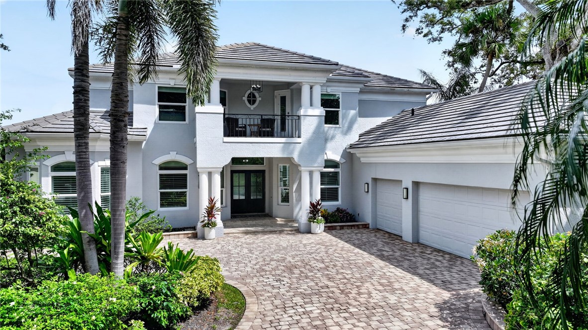 Stucco exterior with a tiled roof, paver driveway, integrated two-car garage, and established landscaping