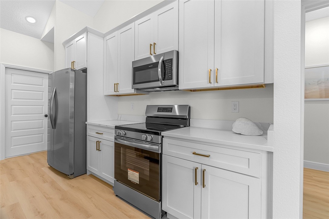 White shaker cabinetry, stainless steel appliances, solid surface countertops, light wood-finish flooring, and vaulted ceiling