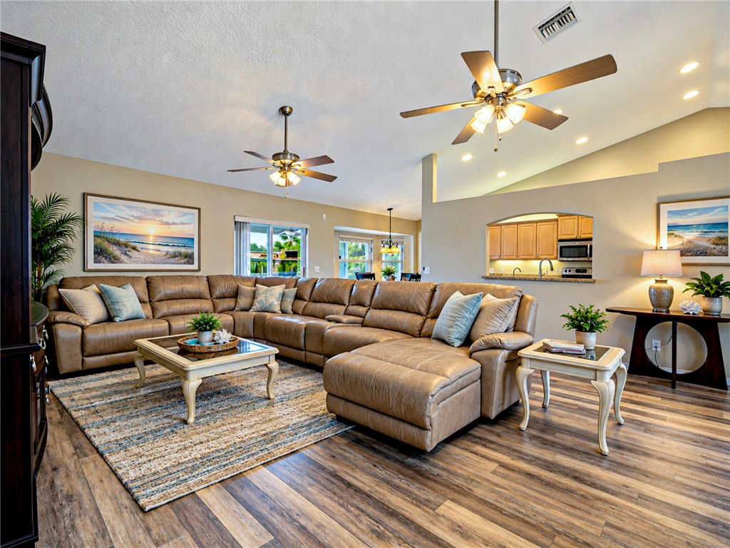 Vaulted ceiling with recessed lighting, wood-finish flooring, two ceiling fans, and an arched pass-through window to the kitchen