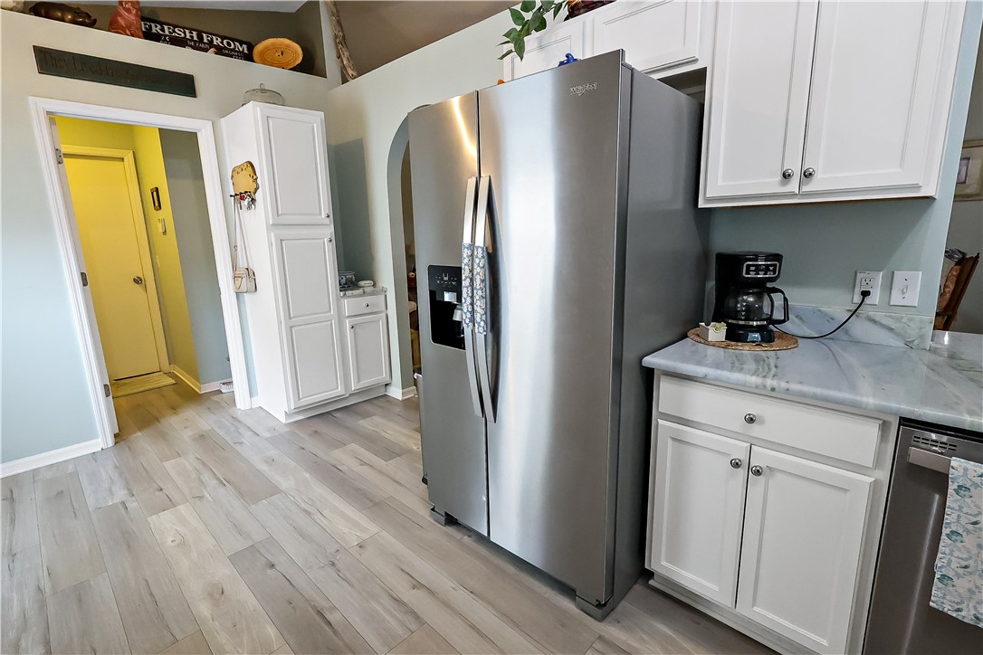 Wood-finish flooring, white cabinetry with silver-tone hardware, stainless steel refrigerator, and light-toned countertops