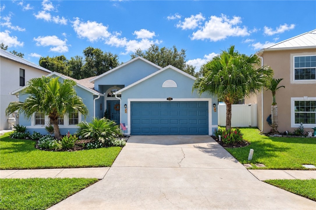 Single-story residence featuring a two-car garage, concrete driveway, and manicured landscaping with mature palm trees
