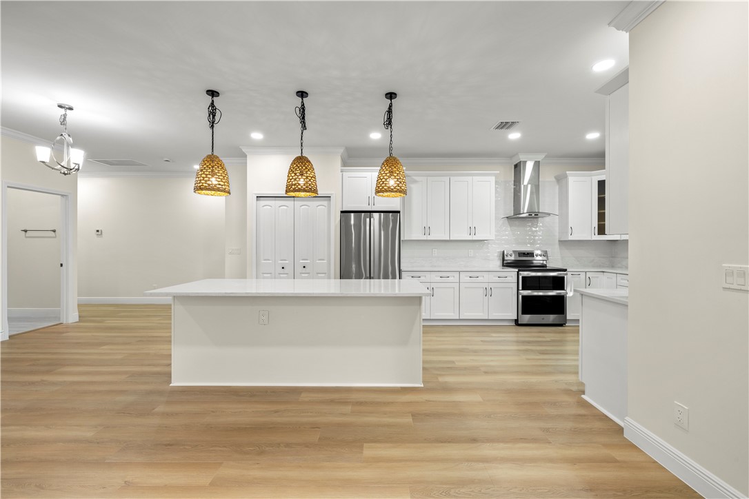 Contemporary kitchen featuring a large central island with a solid surface countertop, stainless steel appliances, white cabinetry, and wood-finish flooring