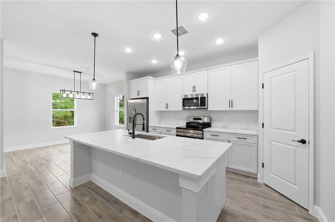 Open-concept kitchen featuring an island with a sink, stainless steel appliances, white cabinetry, and wood-finish flooring
