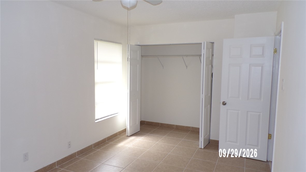 Neutral-toned tile flooring, white walls, built-in closet with bi-fold doors, and a ceiling fan with light fixture