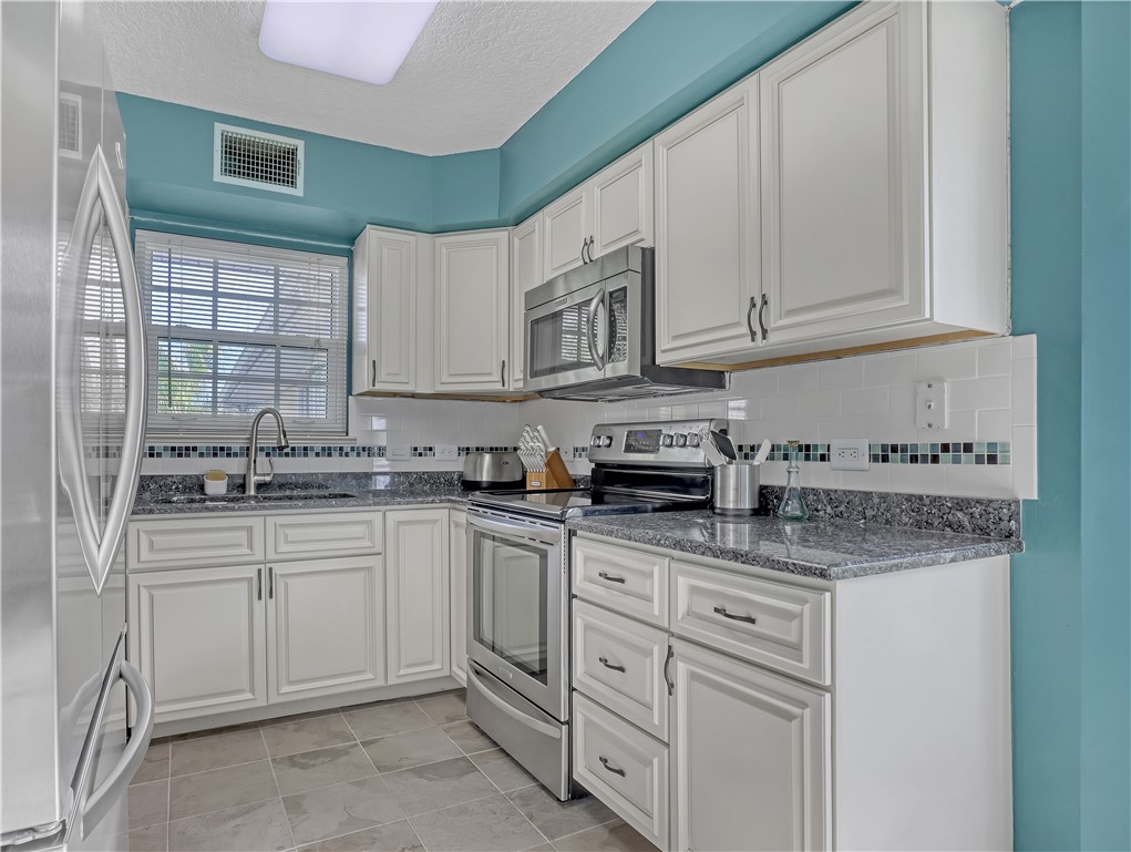 Kitchen featuring white cabinetry, speckled countertops, stainless steel appliances, a tile backsplash, and tile flooring