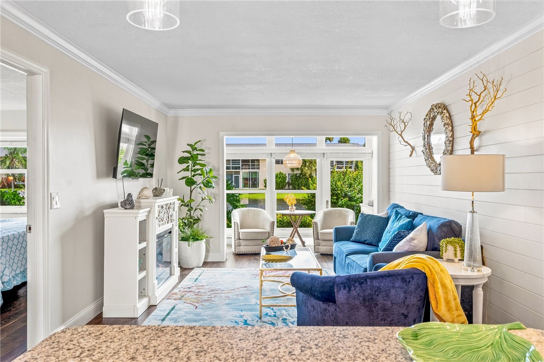 Bright and airy living space with abundant natural light from multi-panel glass doors and windows, white shiplap accent wall, hardwood flooring, and built-in white cabinetry with glass-front storage