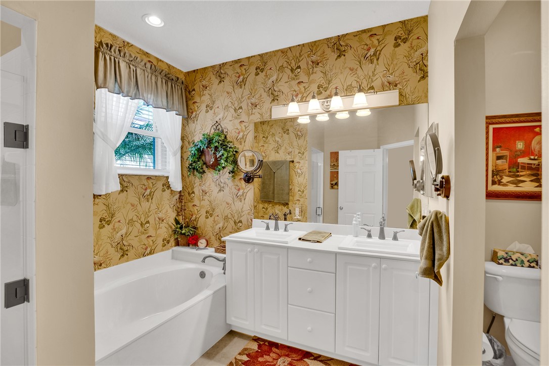Dual sink vanity with white cabinetry and chrome fixtures, built-in soaking tub, recessed ceiling lighting, and a separate water closet