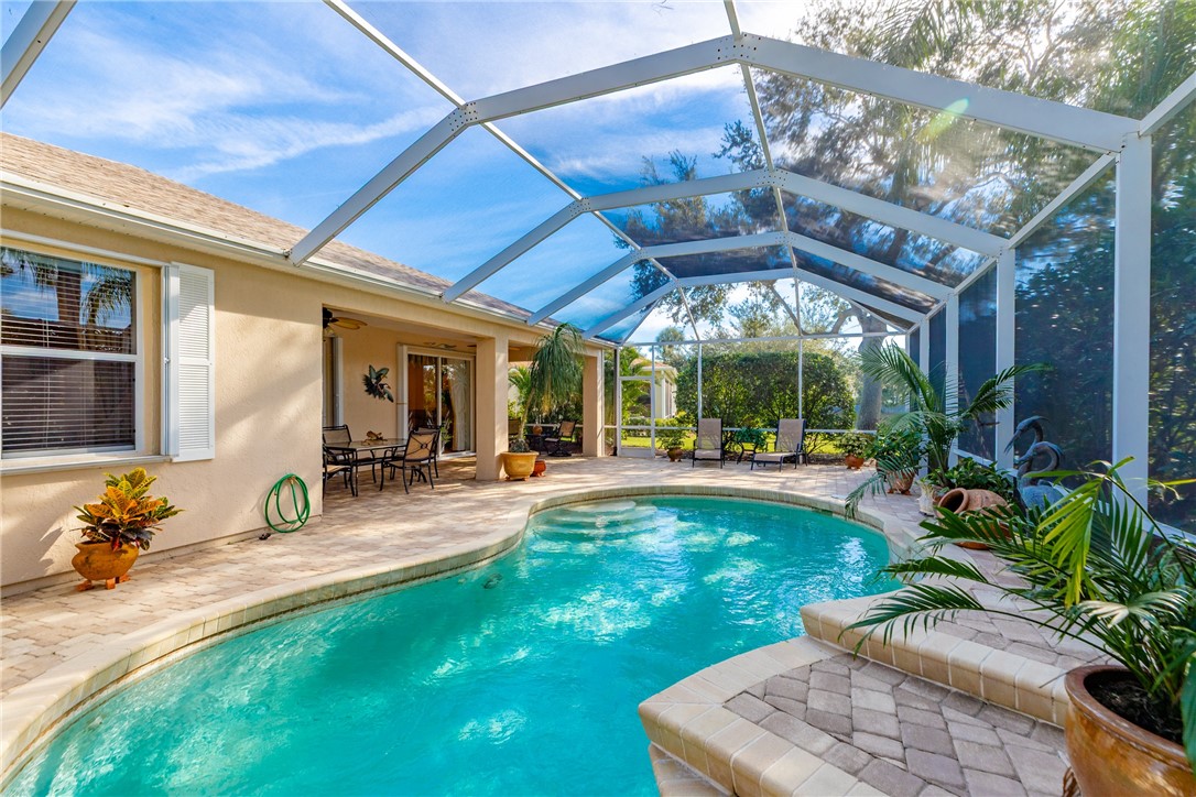 Screened-in outdoor living space with a free-form swimming pool, paver patio, covered lanai, and exterior stucco finish
