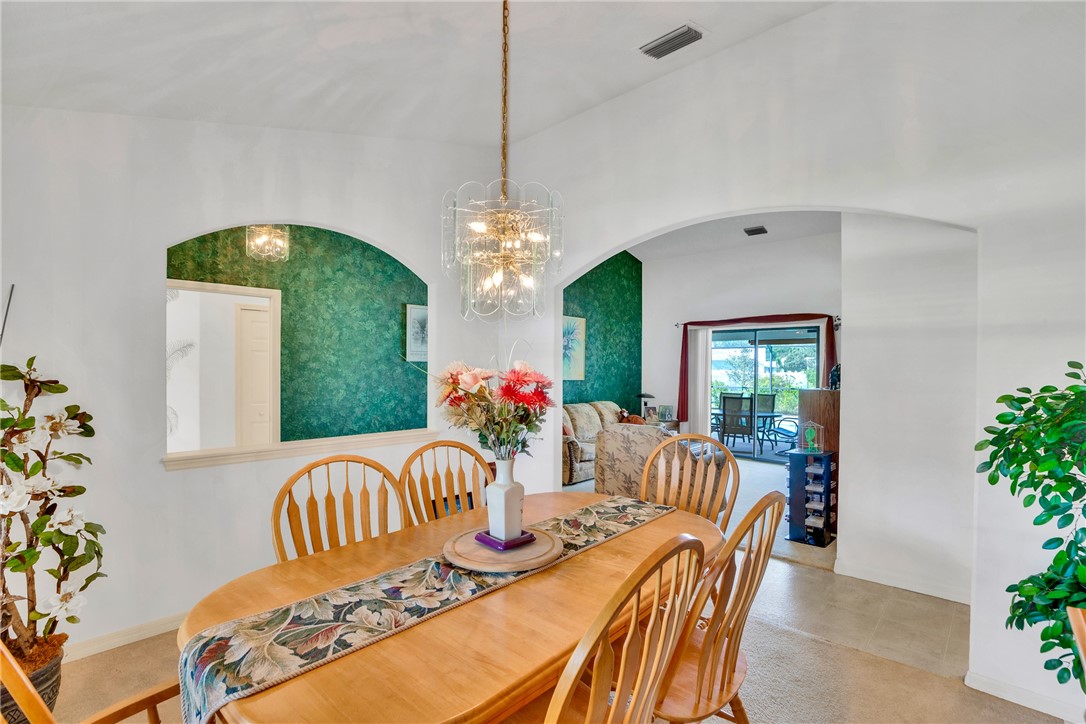 Vaulted ceiling dining area featuring a modern chandelier, arched wall openings, a pass-through window with textured green accent wall, and ceramic tile flooring