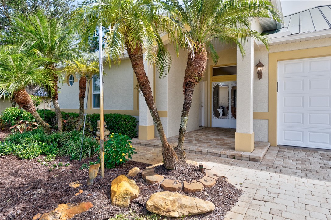Stucco exterior with a paver driveway, an inviting entry porch, a prominent garage door, and lush landscaping