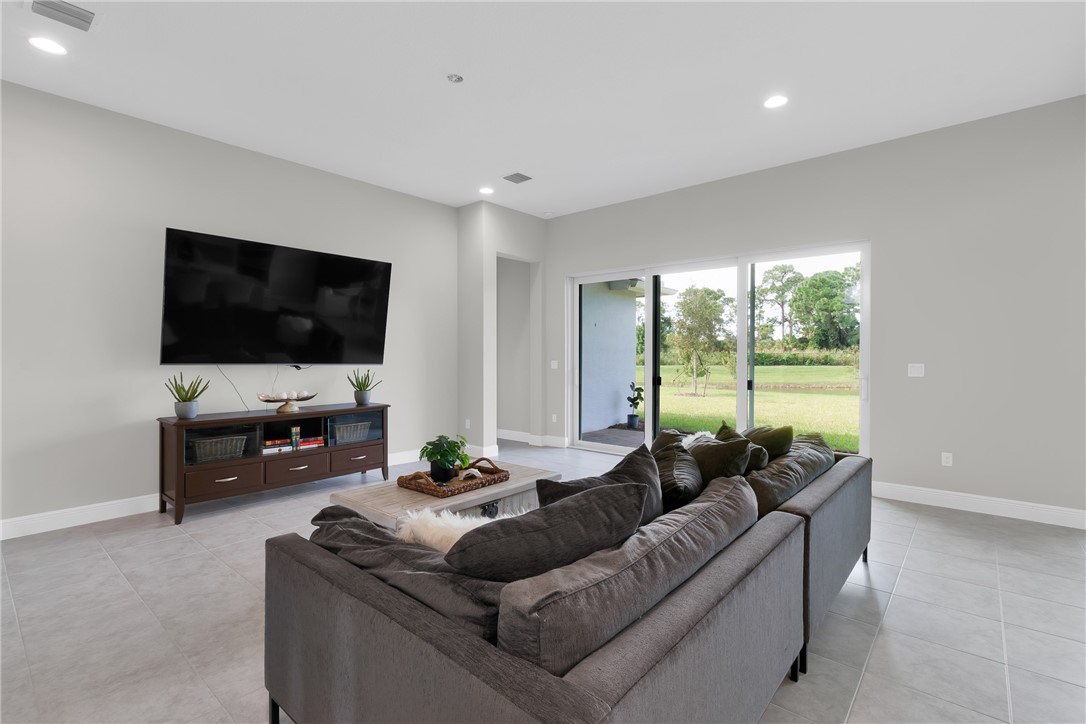 Recessed lighting, light gray wall finishes, gray tile flooring, and sliding glass doors in living room.