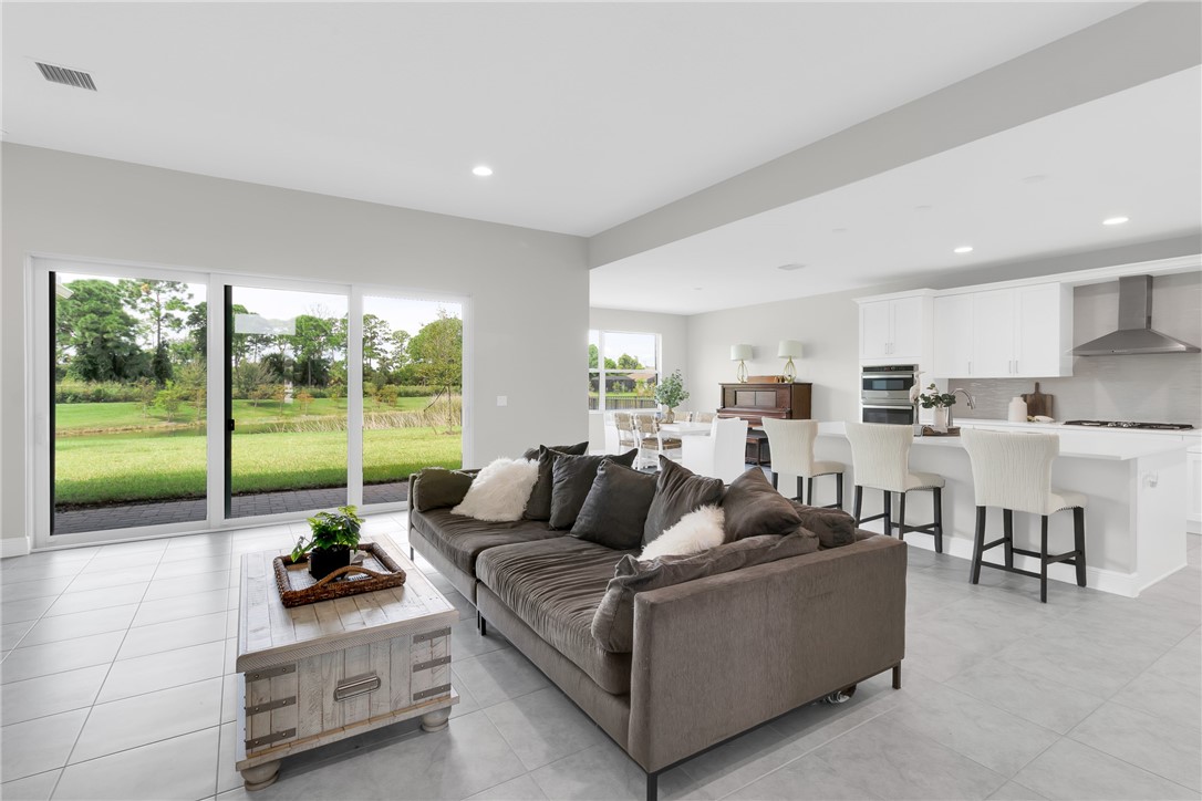Expansive sliding glass doors, contemporary kitchen with white cabinetry, stainless steel range hood, built-in double oven, and large center island with bar stool seating.
