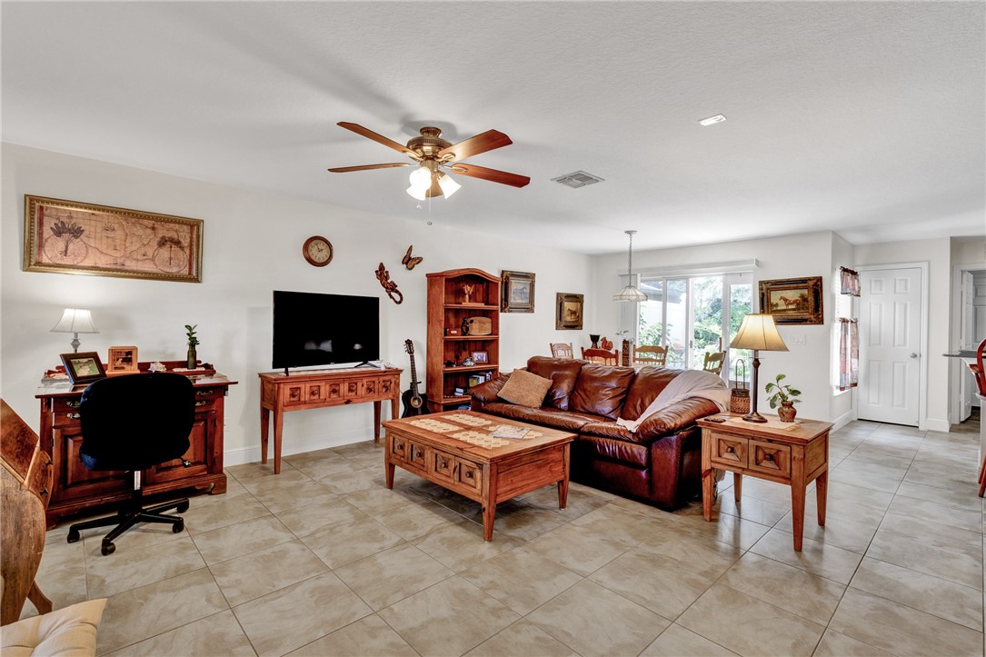 Spacious living area featuring neutral tile flooring, a ceiling fan, and white walls