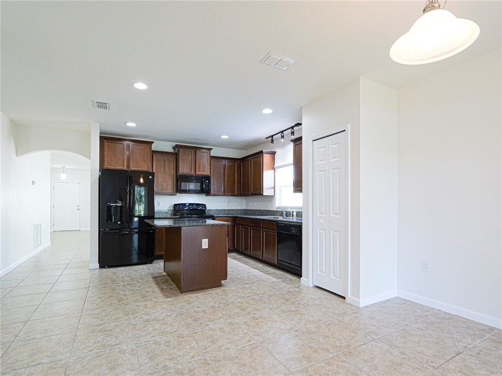 Kitchen featuring wood cabinetry, an island, dark countertops, black appliances, and recessed lighting