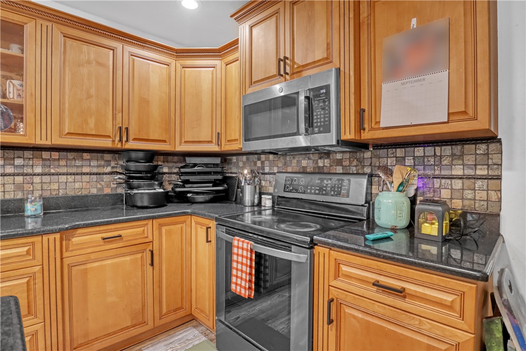 Warm wood cabinetry with crown molding, solid surface countertops, tile backsplash, and stainless steel appliances