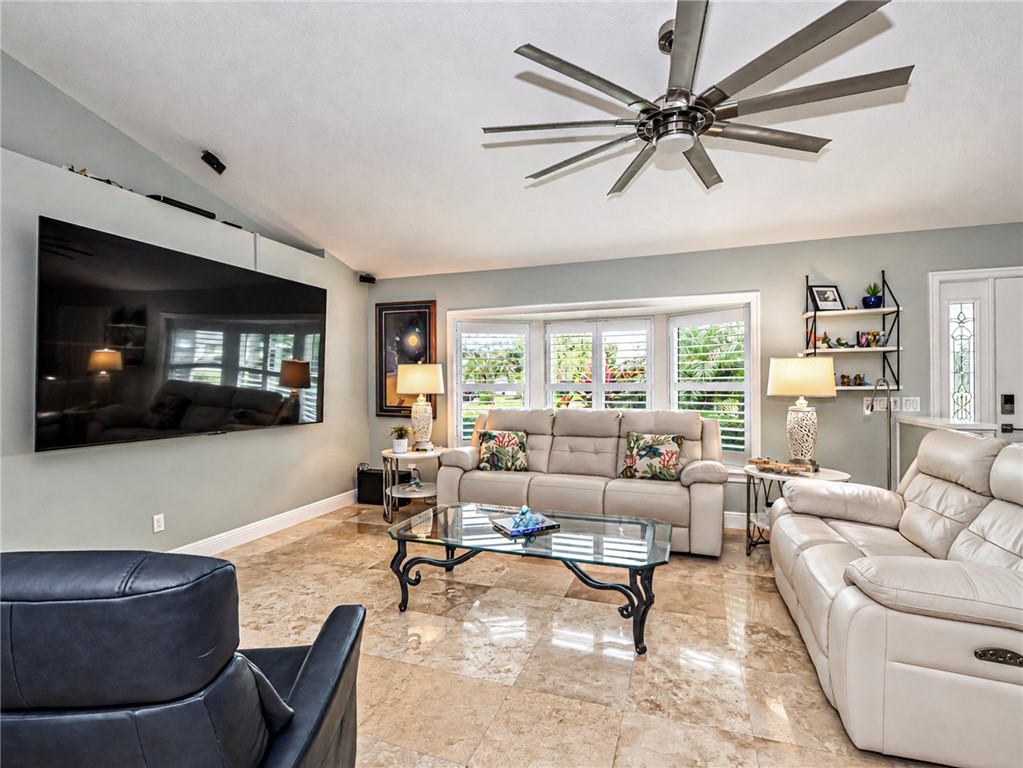 Living area with bay window, plantation shutters, vaulted ceiling, oversized multi-blade ceiling fan.