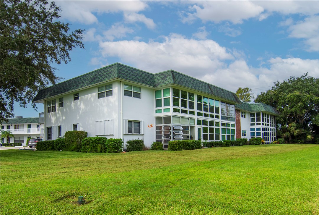 White exterior with green shingle roofing, multiple enclosed patio spaces, and surrounding green lawn