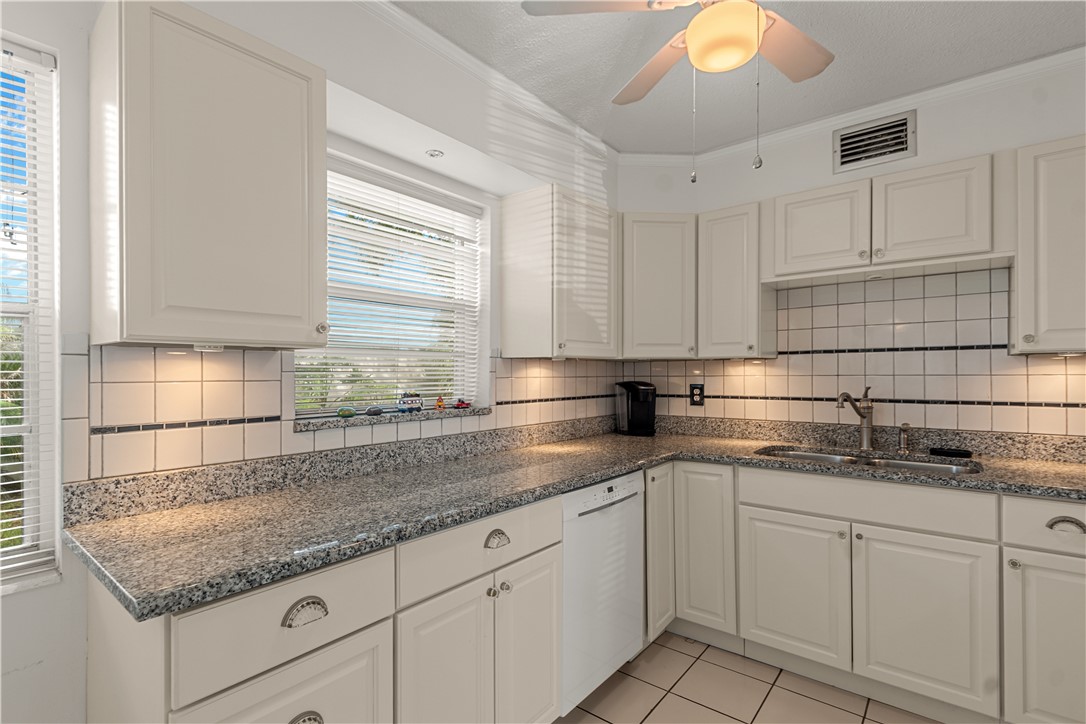 White cabinetry with silver hardware, granite countertops, tile backsplash with accent border, and a stainless steel sink with a gooseneck faucet