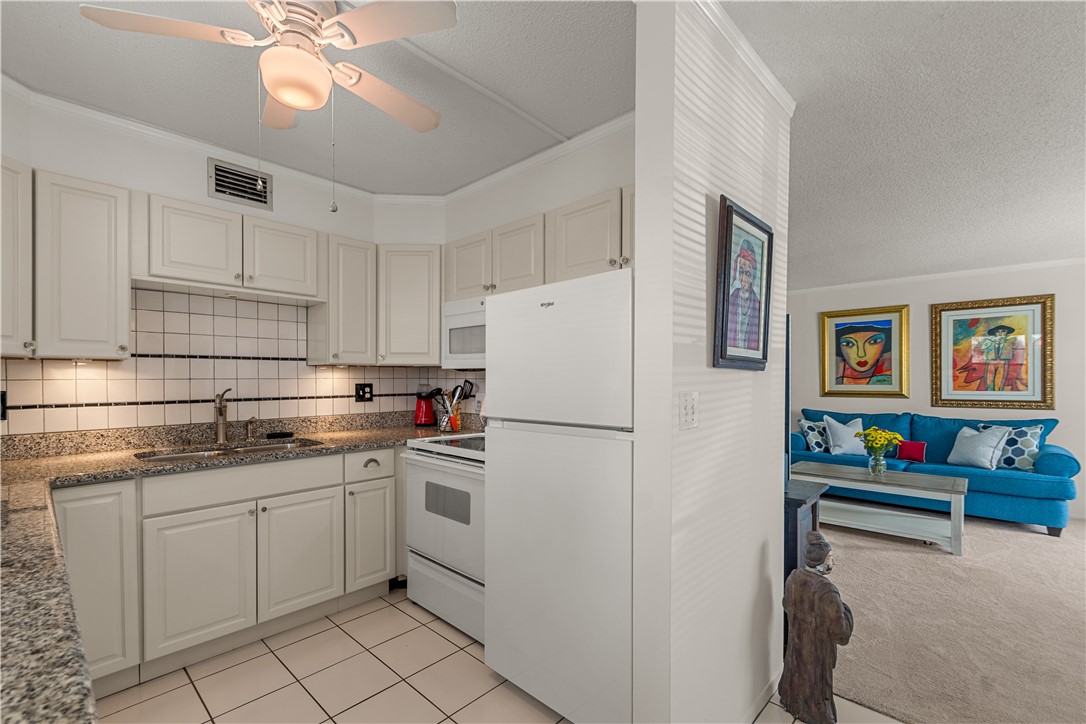 Kitchen featuring white cabinetry, granite-style countertops, tile backsplash, and a ceiling fan with integrated lighting