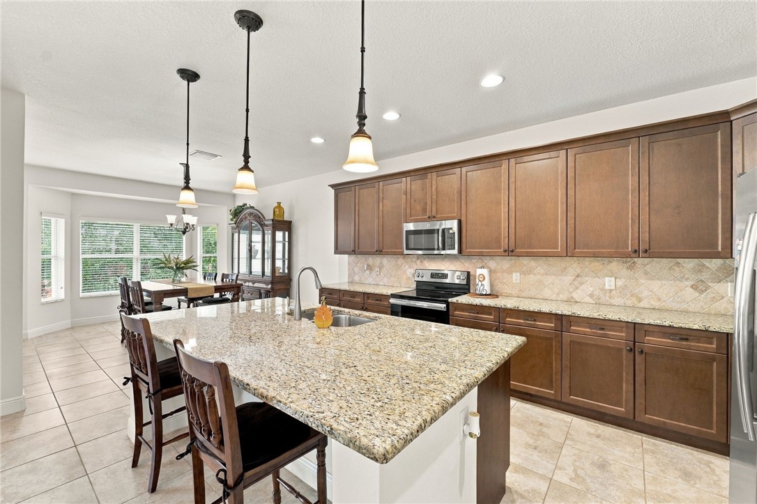 Kitchen featuring a large island with stone countertop, stainless steel appliances, wood cabinetry, and tile flooring