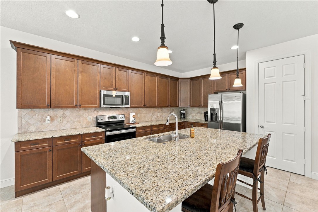 Kitchen featuring recessed lighting, pendant lighting, wood-finish cabinetry, a large kitchen island with counter seating, and stainless steel appliances
