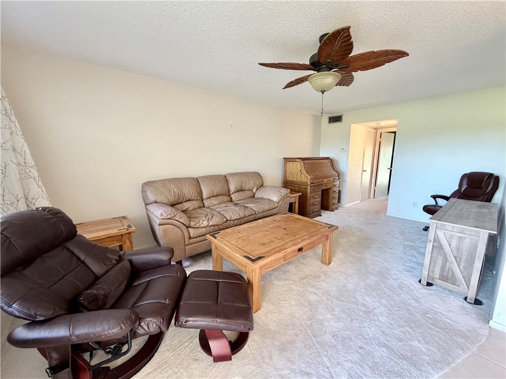 Carpeted living area with a ceiling fan, neutral wall tones, and a doorway