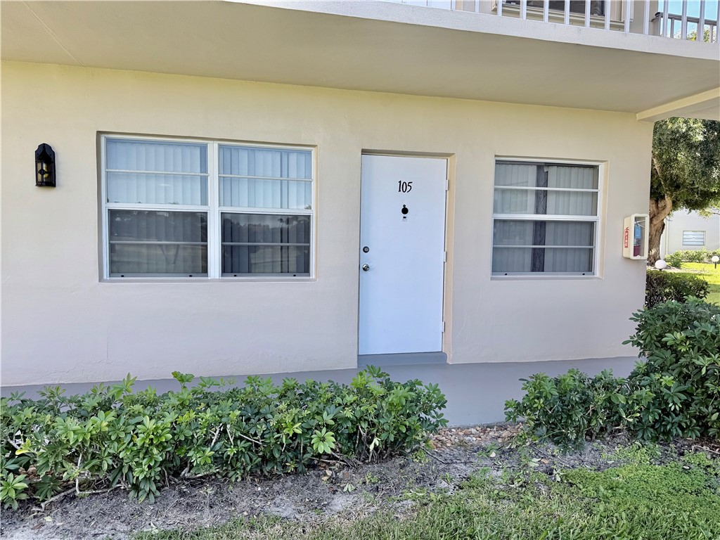 Entry with a white door, exterior wall sconce, and mature landscaping