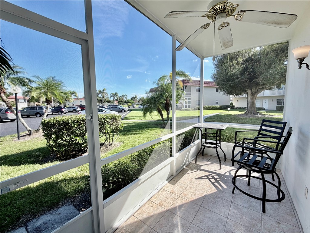 Screened porch with tile flooring and a ceiling fan, featuring a wall-mounted light fixture