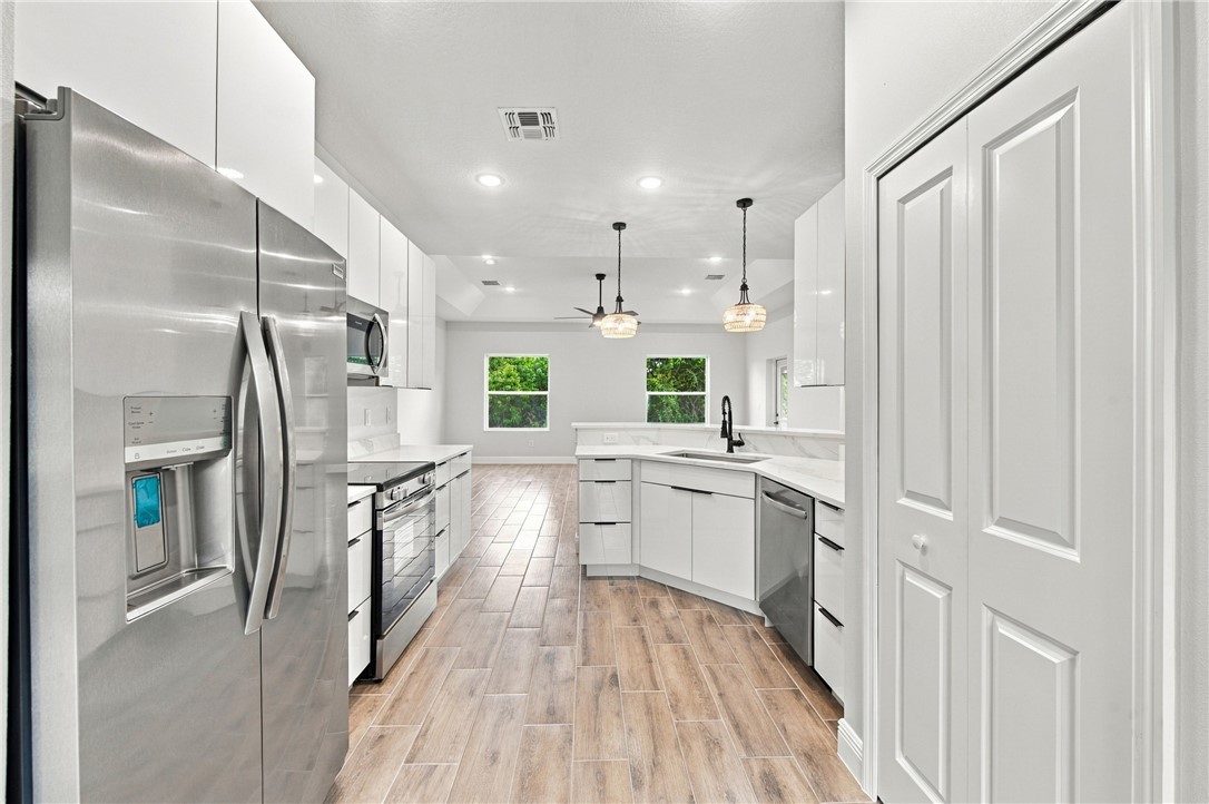 Modern kitchen featuring stainless steel appliances, wood-finish flooring, white cabinetry, recessed lighting, and pendant lighting