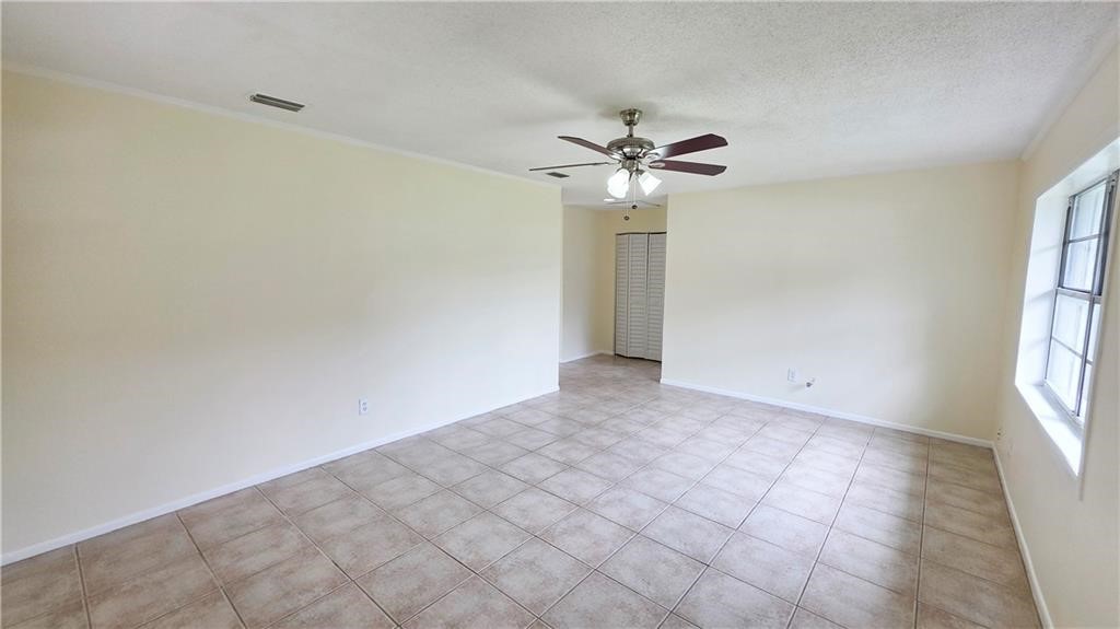 Spacious room featuring tile flooring, neutral wall tones, a ceiling fan with integrated lighting, and a multi-pane window