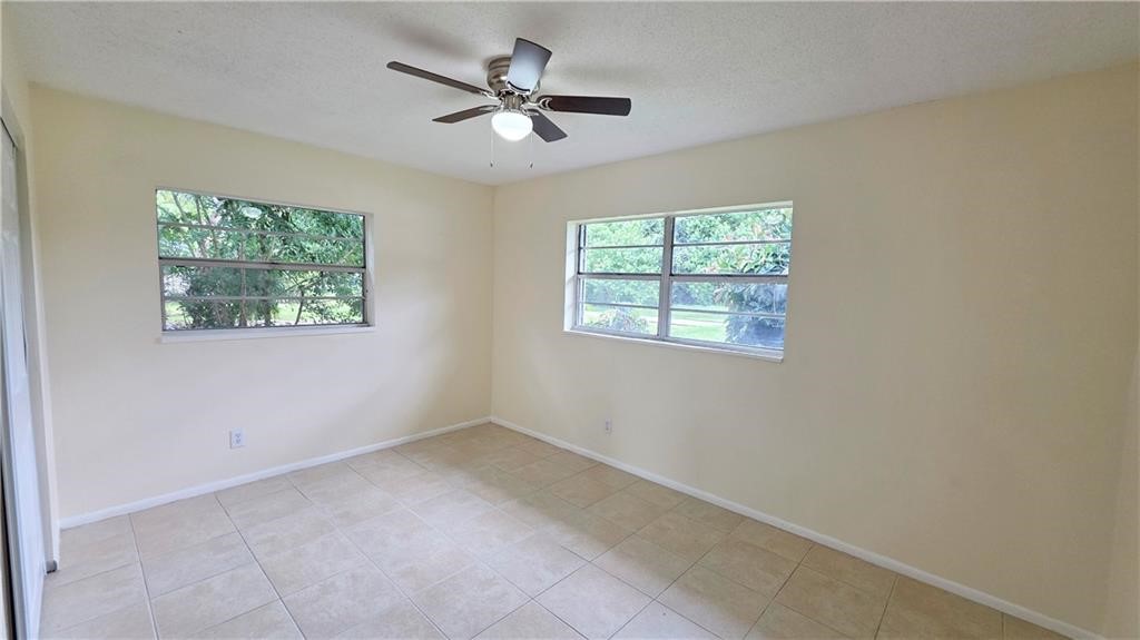 Neutral tone walls, tiled flooring, two windows with security bars, and a ceiling fan with integrated lighting