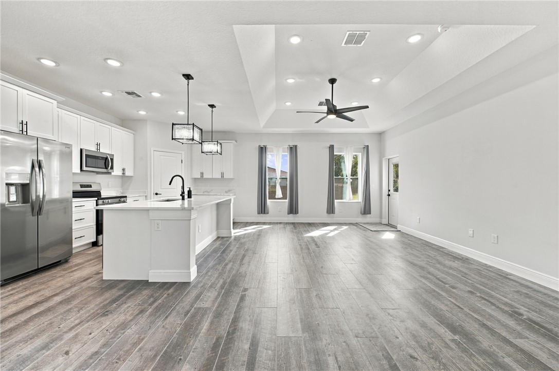 Open-concept living space with wood-finish flooring, white cabinetry, stainless steel appliances, a kitchen island, and a tray ceiling with recessed lighting