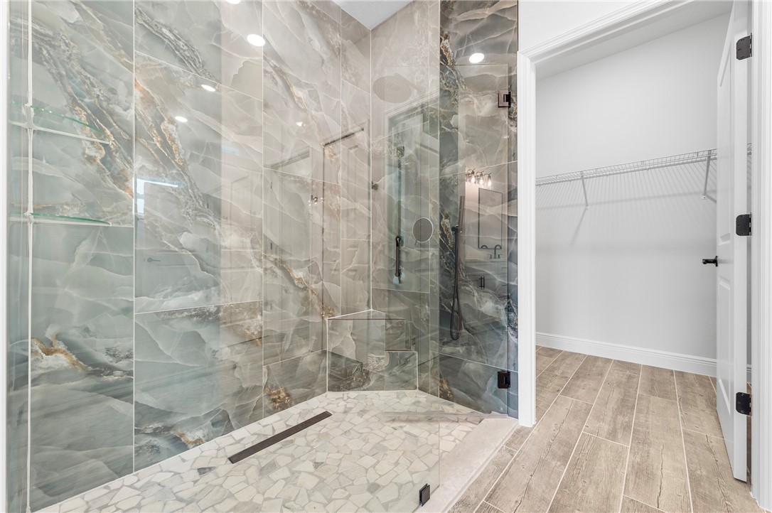 Glass-enclosed shower with full-height stone-finish wall tile, a linear drain, and built-in glass shelving