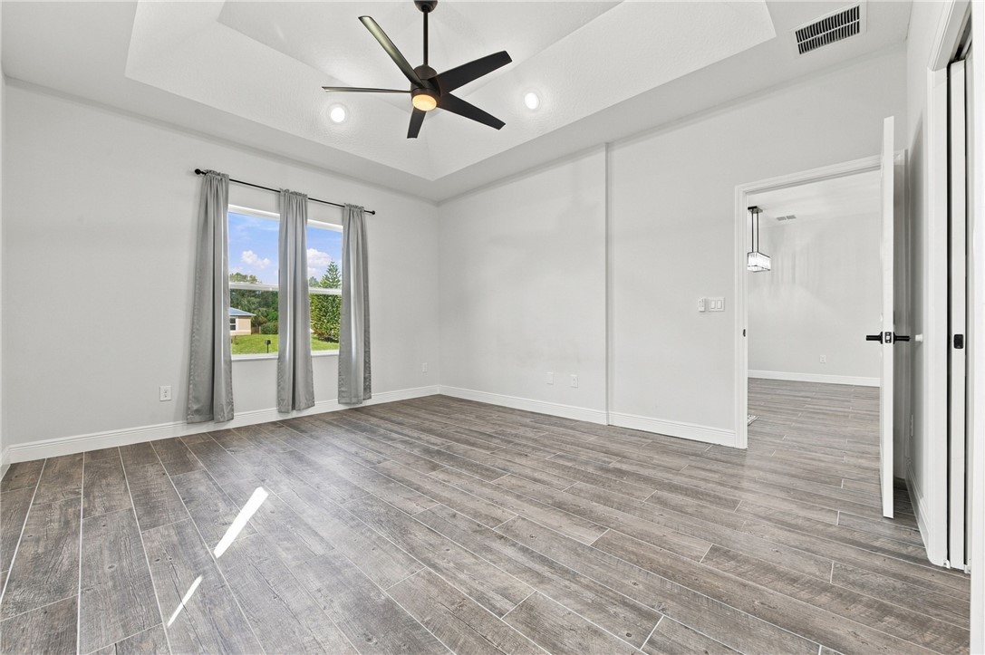 Tray ceiling with recessed lighting and a ceiling fan, wood-finish flooring, and multiple windows