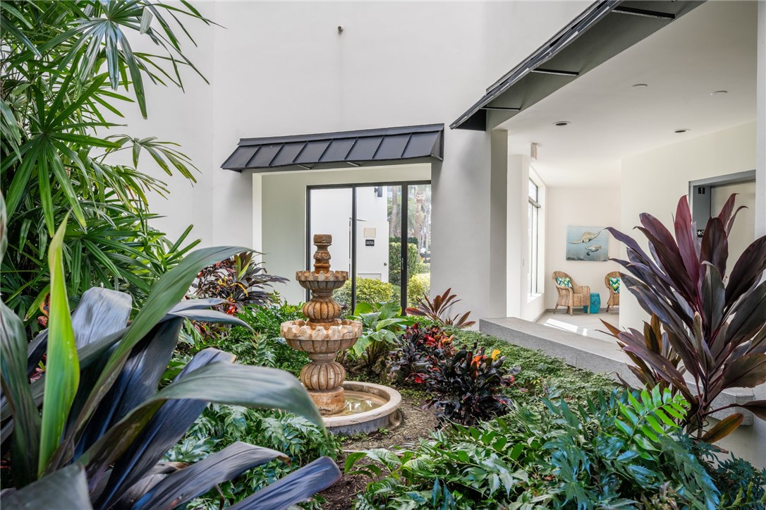 Lush tropical landscaping featuring a tiered fountain, covered entryway, and large windows