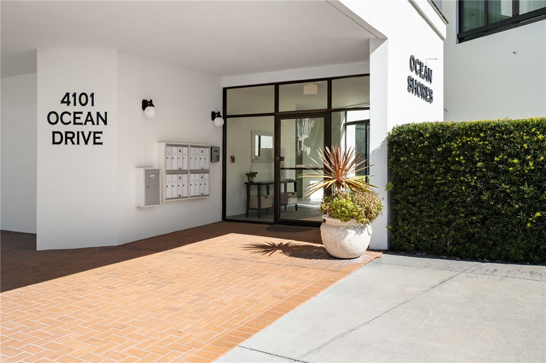 Entryway featuring a paved brick landing, a manicured hedge, and a glass-paneled entry door