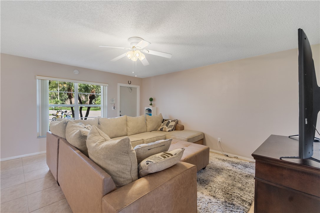 Living area featuring tile flooring, a large window, a ceiling fan with light fixture, and neutral wall tones