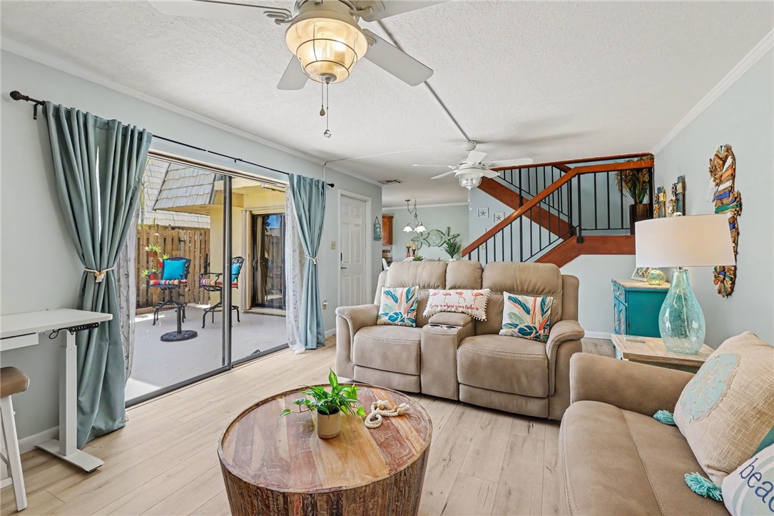 Wood-finish flooring, sliding glass patio doors, two ceiling fans, and a visible staircase with dark railings