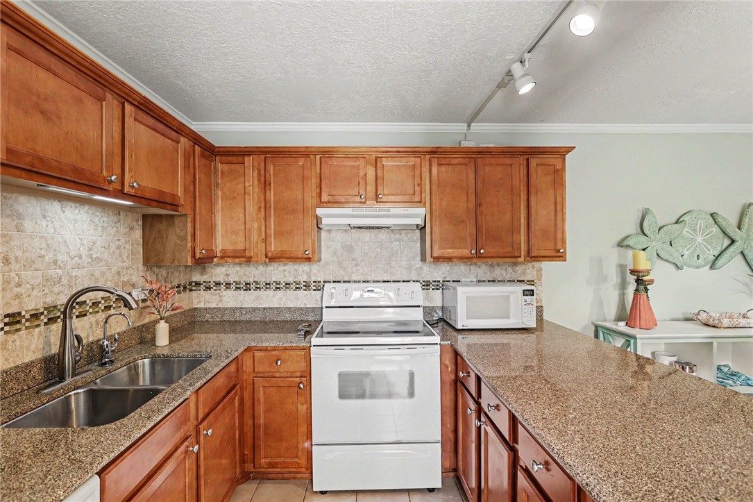 Kitchen featuring wood cabinetry, stone countertops, a tiled backsplash, and a double basin stainless steel sink