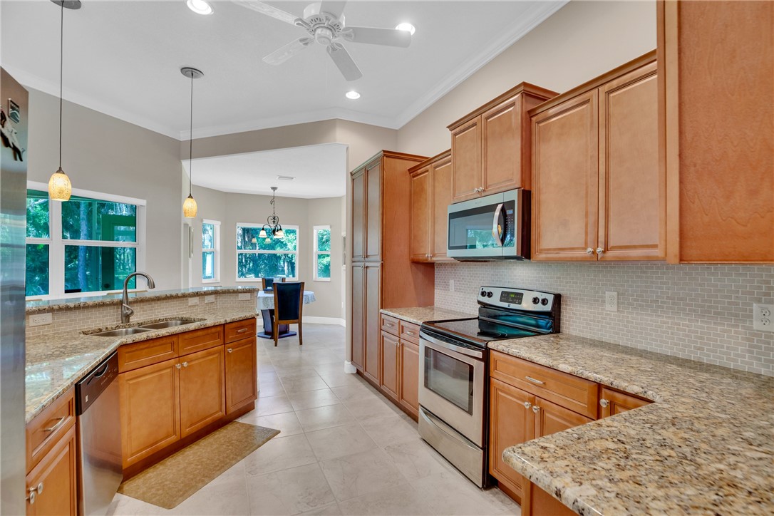 Spacious kitchen featuring extensive cabinetry, stainless steel appliances, granite countertops, tile backsplash, and ceramic tile flooring