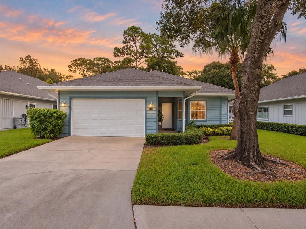 Light blue exterior siding, white garage door, concrete driveway, front yard landscaping, and mature trees