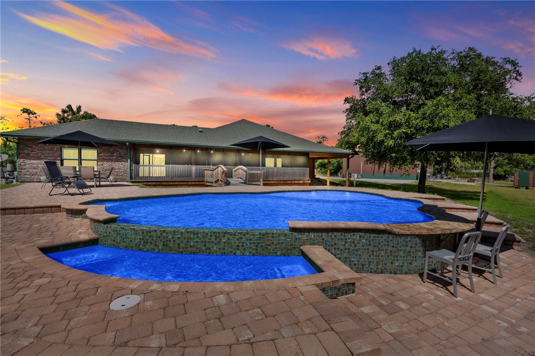 Freeform swimming pool with an integrated spa, surrounded by a paver patio and a raised tile-faced wall